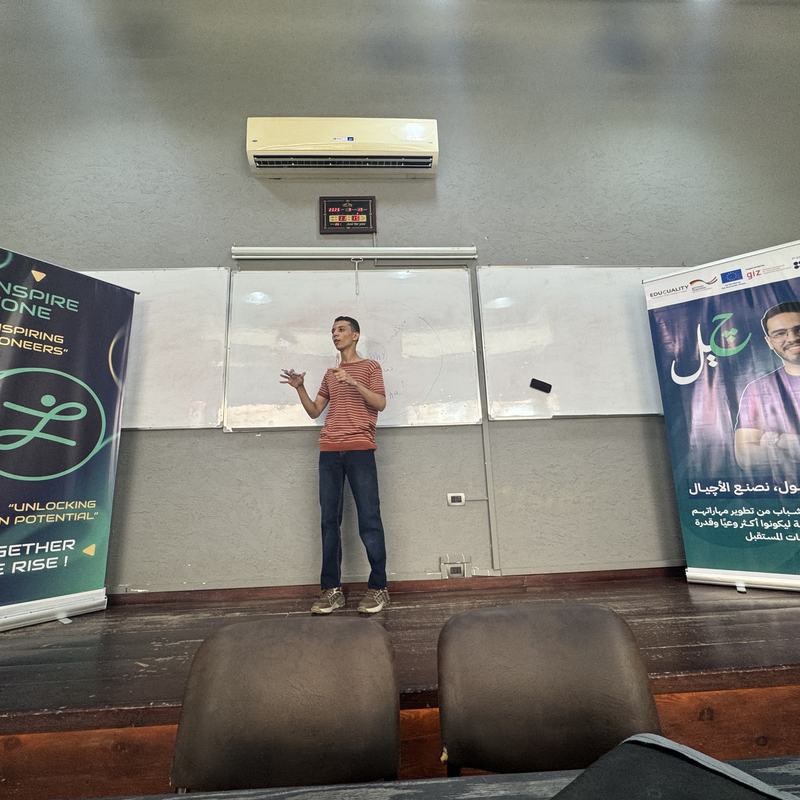 Yousef speaking onstage between two event banners.